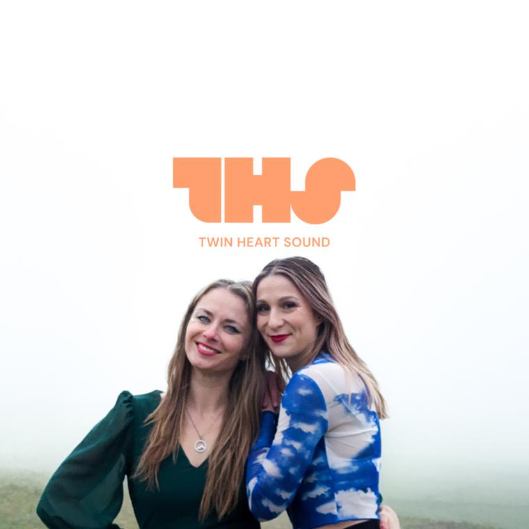 The duo with arms raised in the mist under the Twin Heart Sound logo